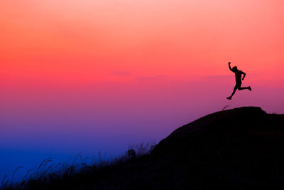 Silhouette person on rock against sky during sunset