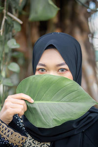 Portrait of woman wearing hijab while covering face with leaf