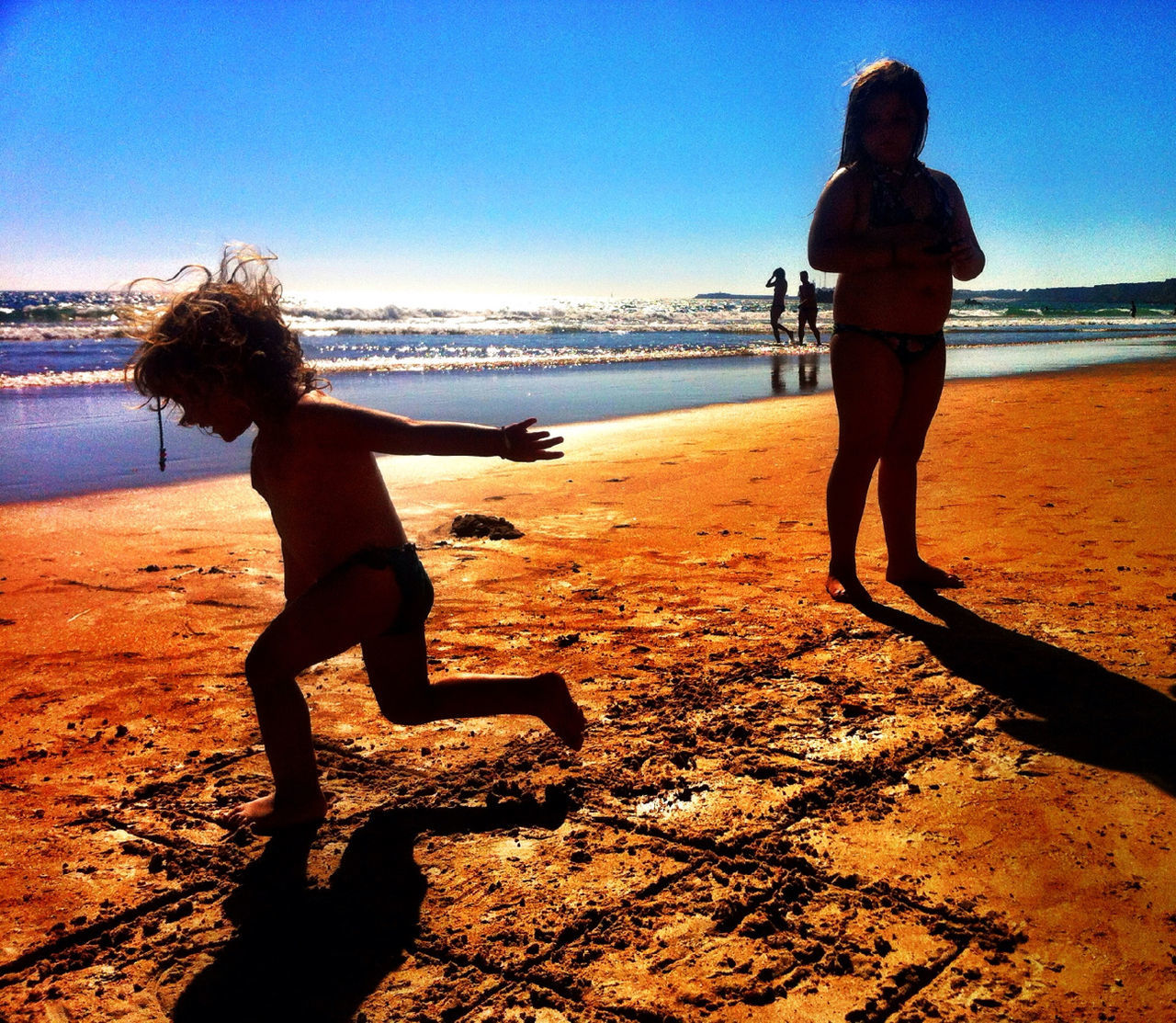 beach, sea, water, shore, full length, sand, clear sky, leisure activity, lifestyles, standing, horizon over water, rear view, blue, sunlight, shadow, walking, silhouette, childhood