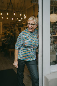 Senior female owner laughing while standing near store doorway