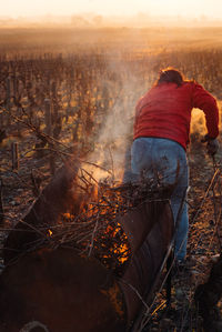 Rear view of man with arms raised on field against sky during sunset