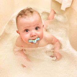 High angle portrait of baby boy with pacifier in mouth taking bath