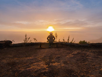 Rear view of woman walking on field against sky during sunset