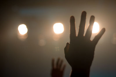 Cropped hands of people against illuminated lights in concert