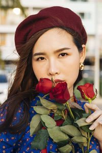 Portrait of young woman holding rose standing against buildings