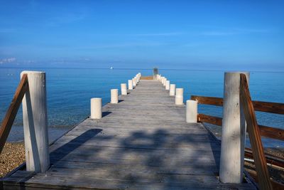Wooden pier over sea against blue sky