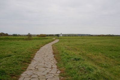 Dirt road amidst field against sky
