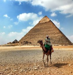 Man riding camel against pyramid at desert