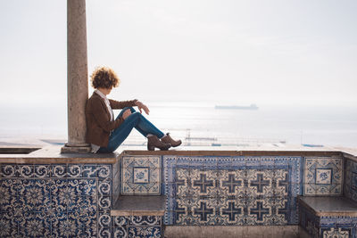 Woman sitting by text on sea against sky