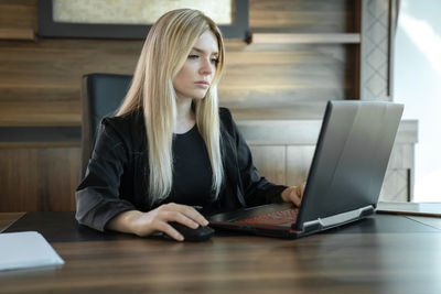 Blonde girl in business clothes sits in front of laptop in office, concept of online  work.