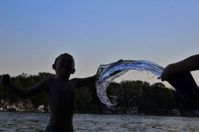 Boy splashing water at lake against clear sky