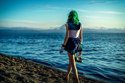 Rear view of woman standing at beach against sky during sunset