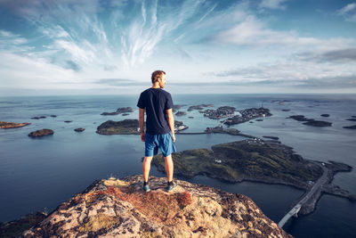 Rear view of man standing on cliff with sea in background against sky