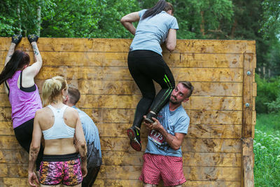 Full length of friends standing against wooden wall