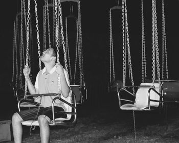 Smiling young man sitting on chain swing ride at night