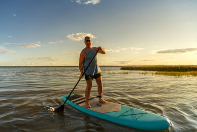 Rear view of man standing on boat on sea against sky