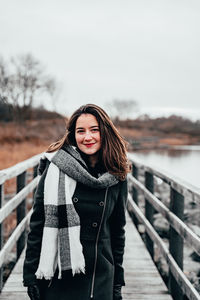 Portrait of young woman standing on footbridge against clear sky