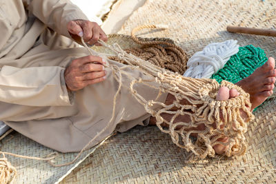 Old man is knitting traditional fishing net, hands in frame