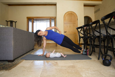 Full length of smiling mother exercising while daughter lying on exercise mat at home