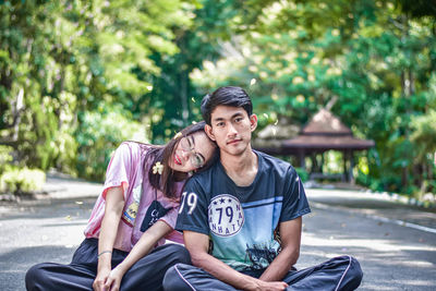 Young couple sitting on footpath while looking at camera