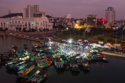 Aerial view of illuminated boats at harbor by buildings in city at night