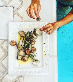 Cropped hand of woman picking seafood from tray by swimming pool