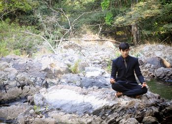 Businessman doing yoga on rock by stream at forest