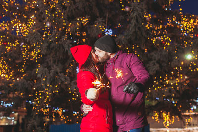 Couple kissing while holding sparkler against illuminated tree