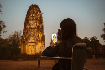 Rear view of woman sitting against built structure against sky