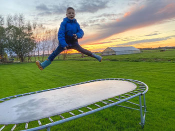 Man jumping on land against sky during sunset