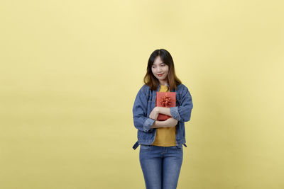 Portrait of smiling young woman standing against yellow background