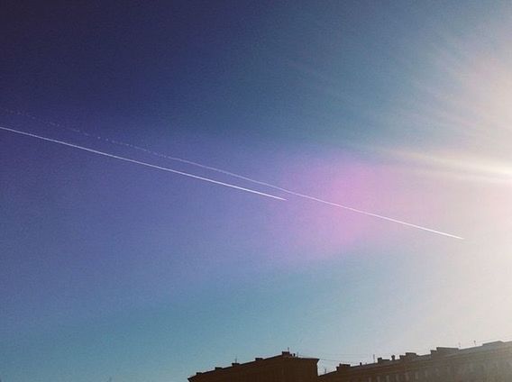 low angle view, vapor trail, built structure, architecture, blue, building exterior, sky, copy space, sun, sunlight, clear sky, outdoors, high section, sunbeam, rainbow, no people, nature, day, scenics, lens flare