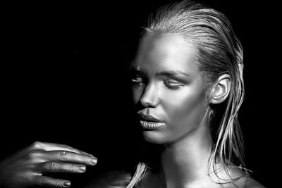 Close-up of young woman with body paint standing against black background