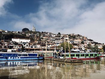 Boats moored at harbor by buildings against sky