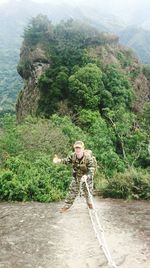 Portrait of army soldier holding rope showing thumbs up while standing against mountain