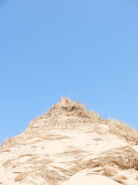 Low angle view of sand dune against clear blue sky