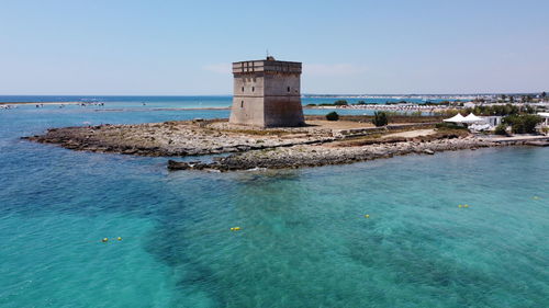 Lighthouse by sea against clear sky