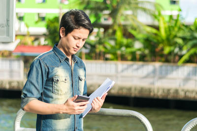 Young man using mobile phone while looking at camera