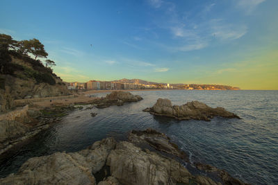 Rocks on sea shore against sky during sunset