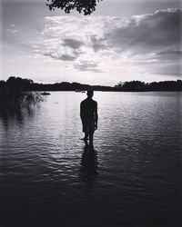 Rear view of silhouette man standing in lake against sky