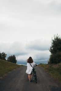 Rear view of woman riding bicycle on road against sky