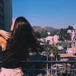 Rear view of woman with long hair standing against cityscape