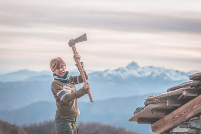 Portrait of angry woman holding axe against sky