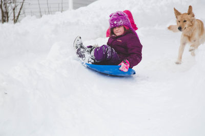 Portrait of girl sliding on sled with golden retriever