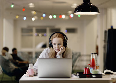 Businesswoman listening music while working late on laptop in creative office