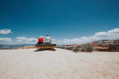 Rear view of men sitting on beach against sky