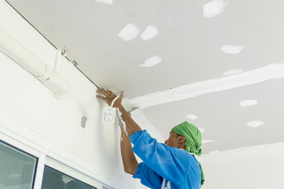 Low angle view of woman working on ceiling