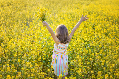 Rear view of girl holding flower with arms raised standing in field