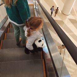 High angle view of daughter holding stuffed toy with mother on escalator in shopping mall