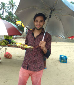 Portrait of smiling young woman holding umbrella standing in rain